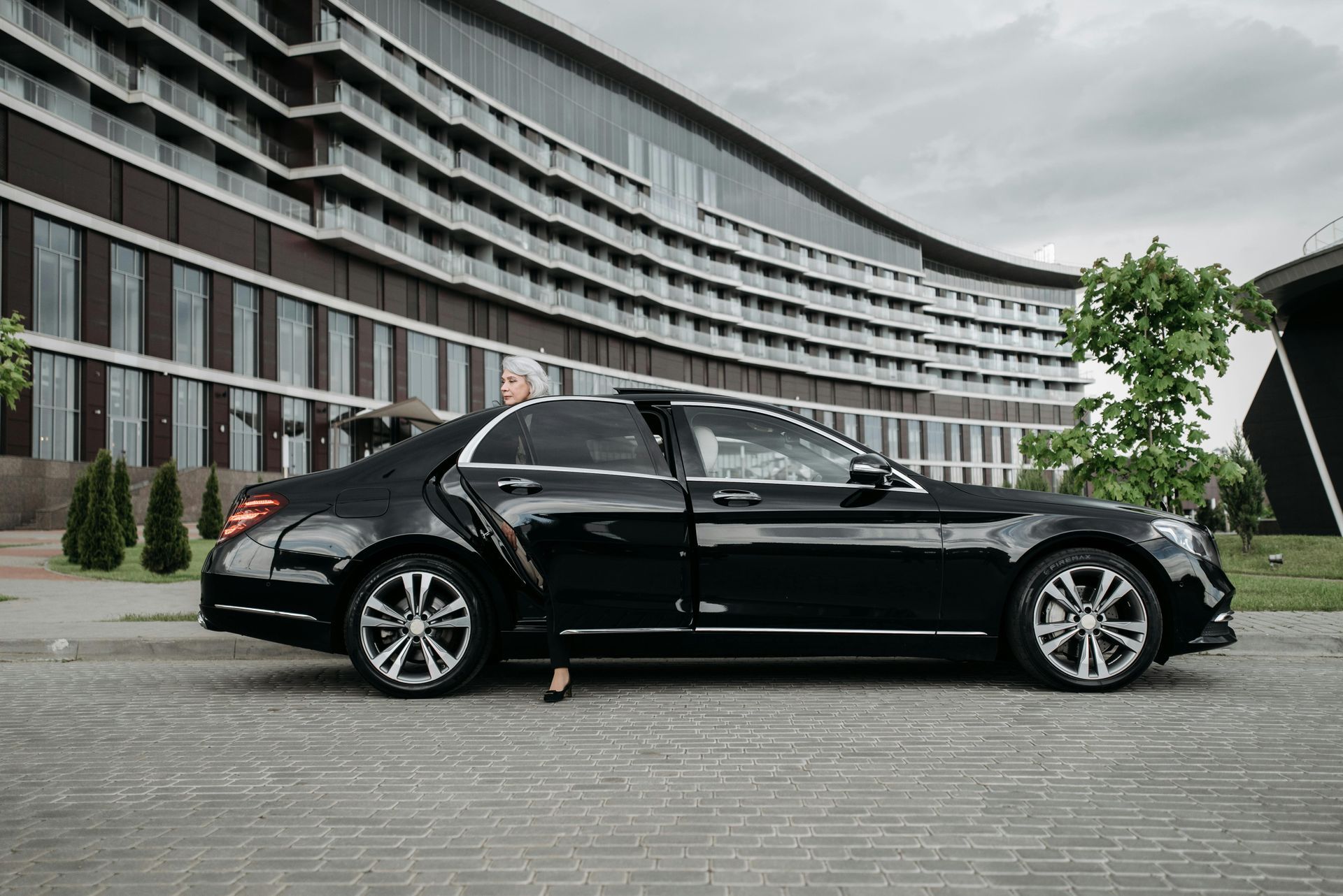 Black sedan parked in front of a modern building, a person partially visible beside the car.