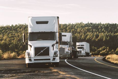 A row of semi trucks are driving down a curvy highway.