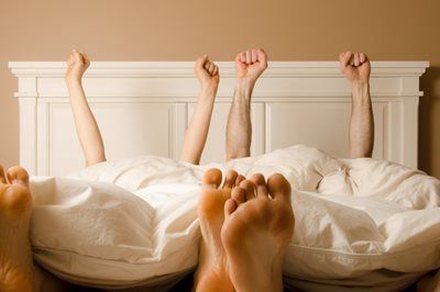 Couple in bed, stretching up arms with toes peaking out from under the blankets