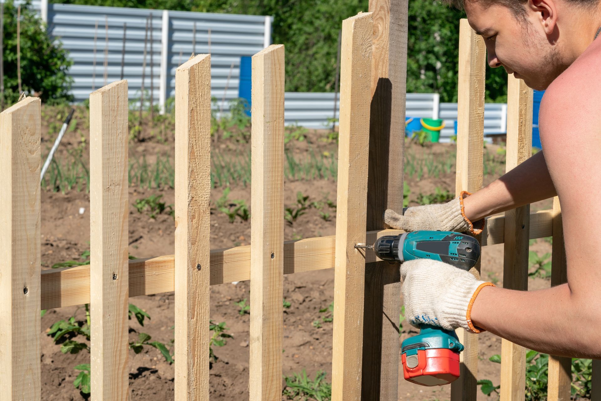 KKR worker repairing wooden fence outside of garden