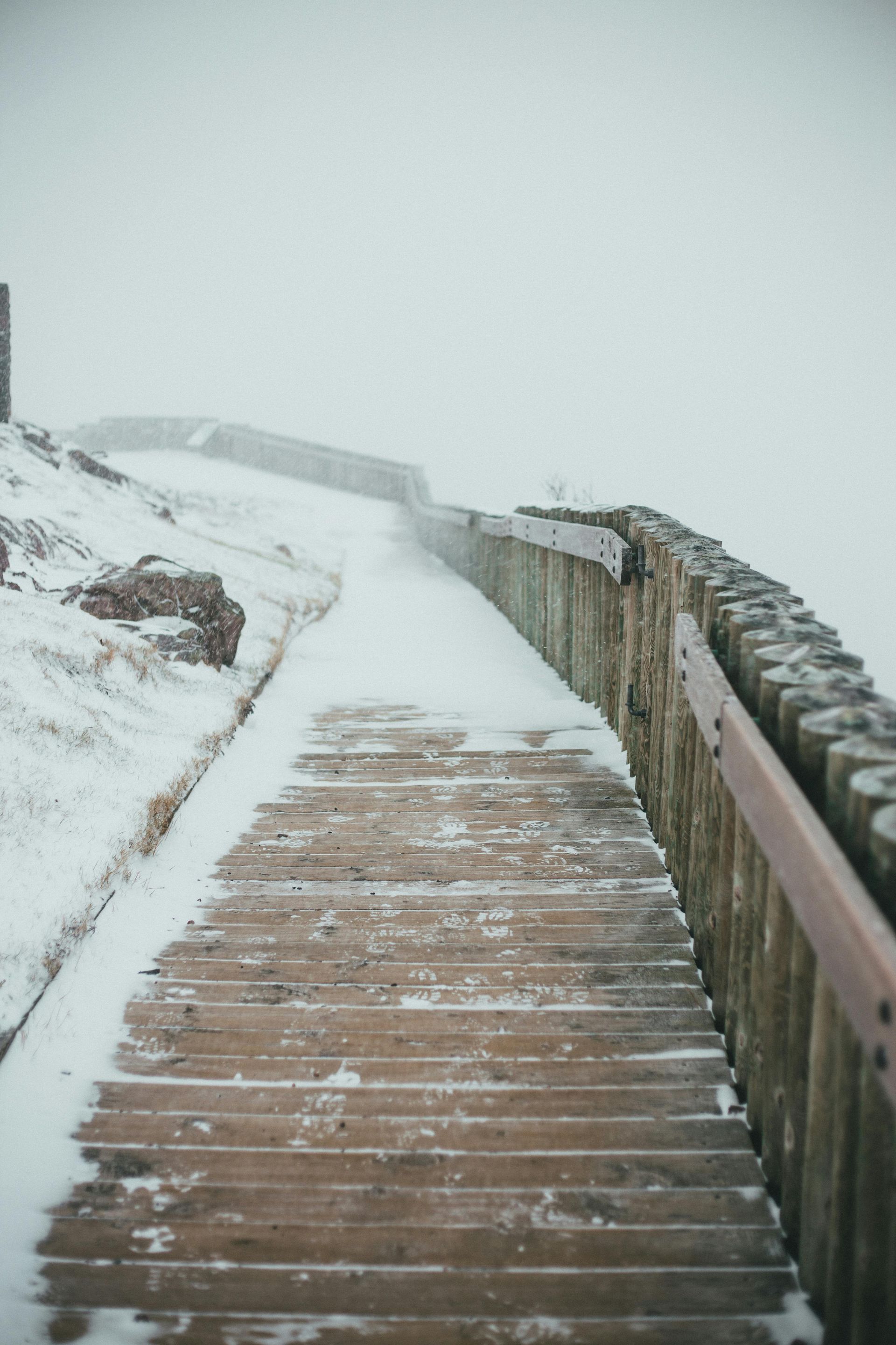 Snow-covered wooden deck with railings in winter, showing weathered boards