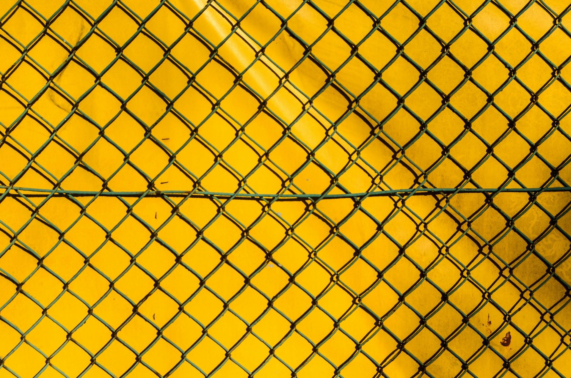 Black chain link fence with diamond mesh pattern against yellow background