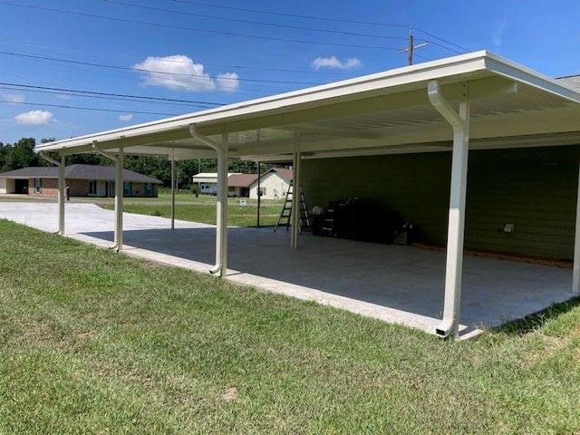 A carport is sitting in the middle of a grassy field next to a house.