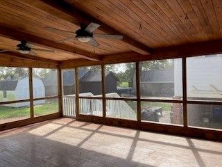A screened in porch with a lot of windows and a ceiling fan.