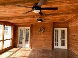 A screened in porch with a ceiling fan and french doors.