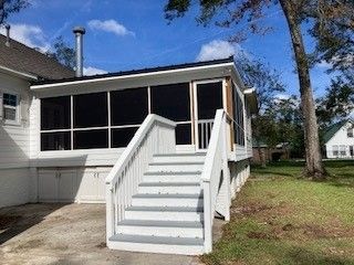 A white house with a screened in porch and stairs leading up to it.