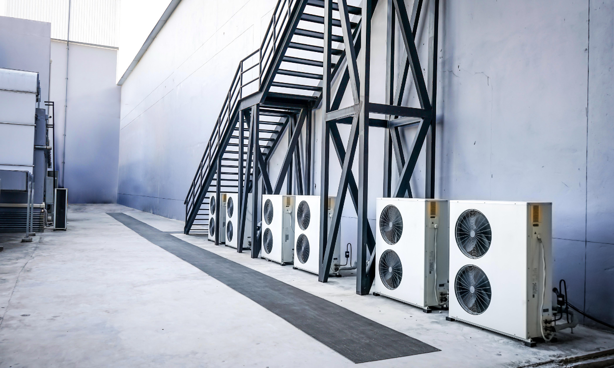 Row of white air conditioning units outside a building, with black metal stairs.