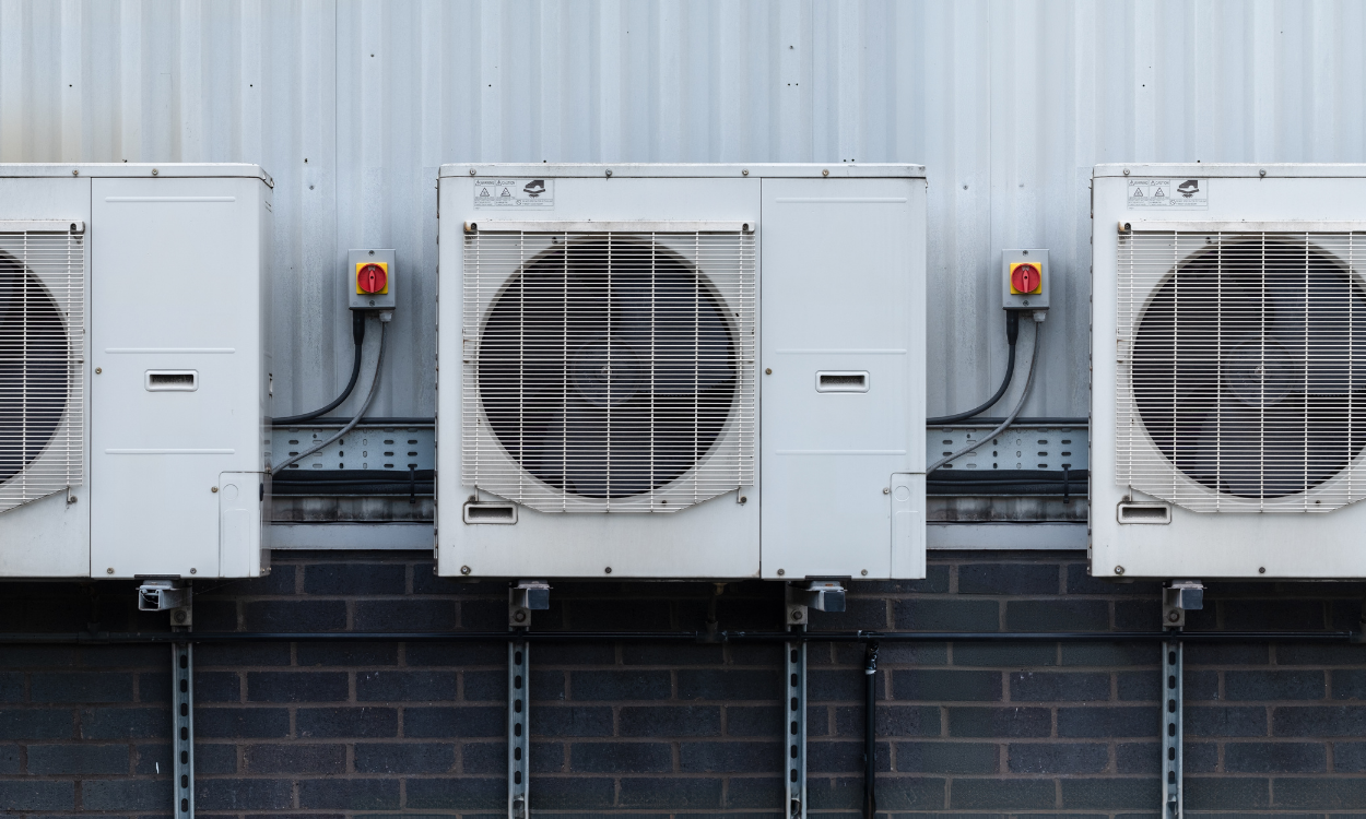 Three white air conditioning units mounted on a gray and black brick wall.