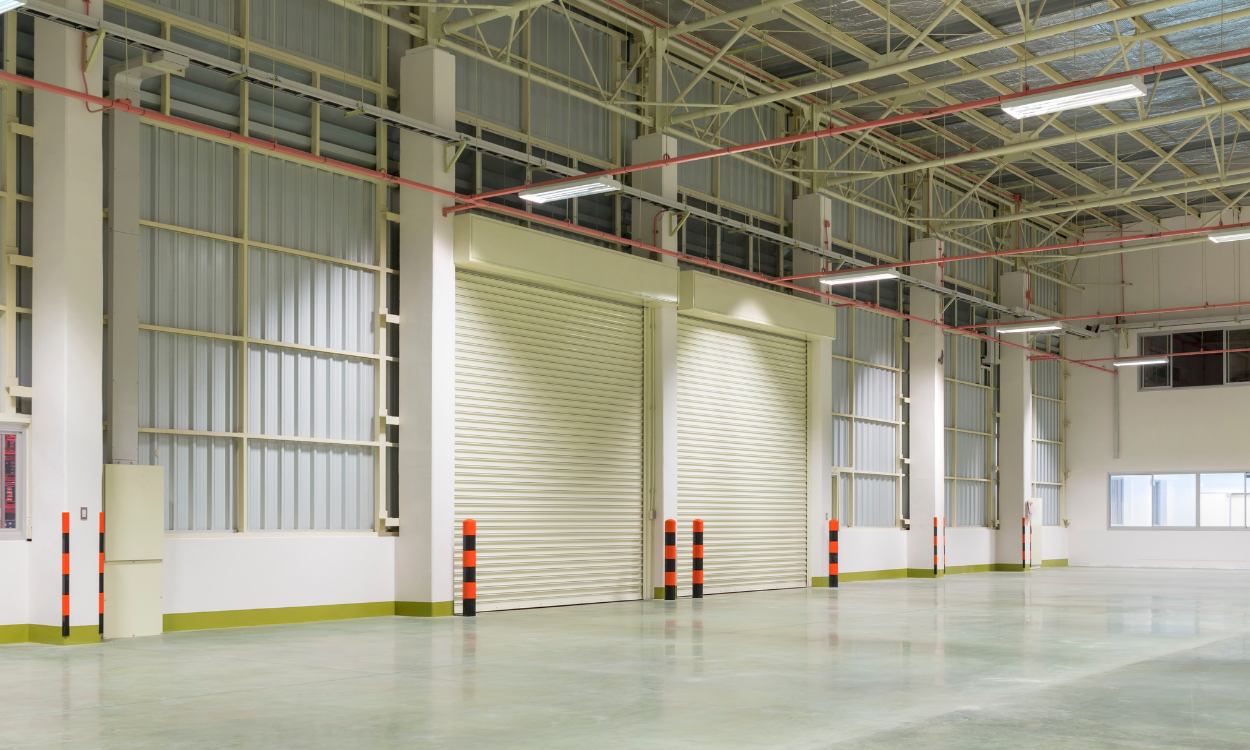 Empty industrial warehouse with roll-up doors, metal siding, and concrete floor.