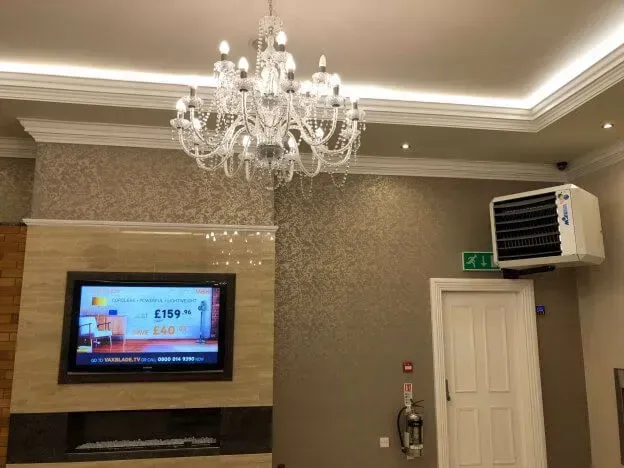 A living room with a chandelier hanging from the ceiling and a warm air heater on the wall