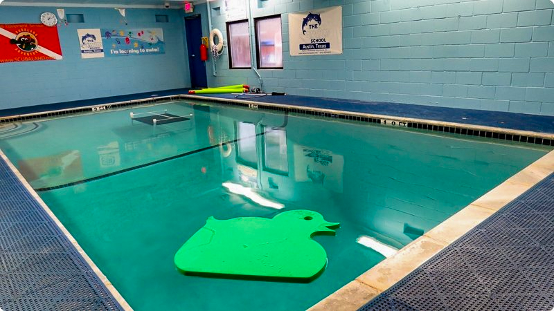 Indoor swimming pool with teal water, a green duck-shaped float, and blue tiled surroundings.