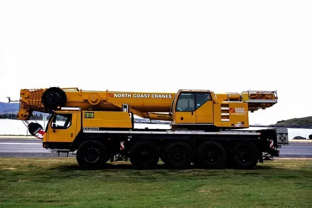 A Large Yellow Crane Is Parked in A Grassy Field — North Coast Cranes In Coffs Harbour, NSW