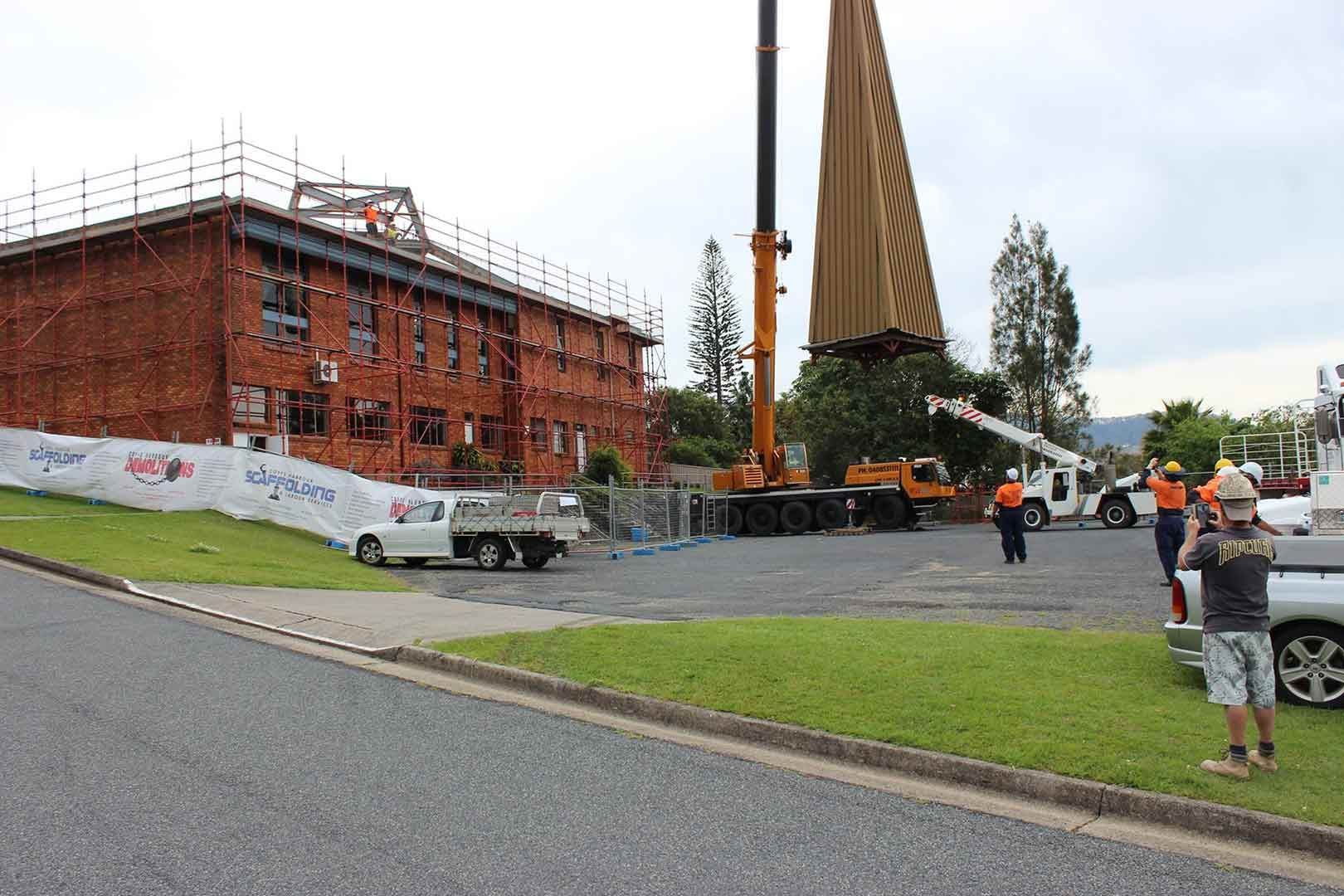 A Crane Is Lifting A Large Object In Front Of A Building Under Construction — North Coast Cane in Woolgoolga, NSW
