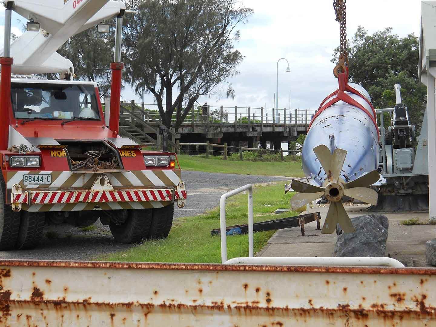 A Red And White Truck Lifting A Metal With Propeller In It — North Coast Cranes In Macksville, NSW