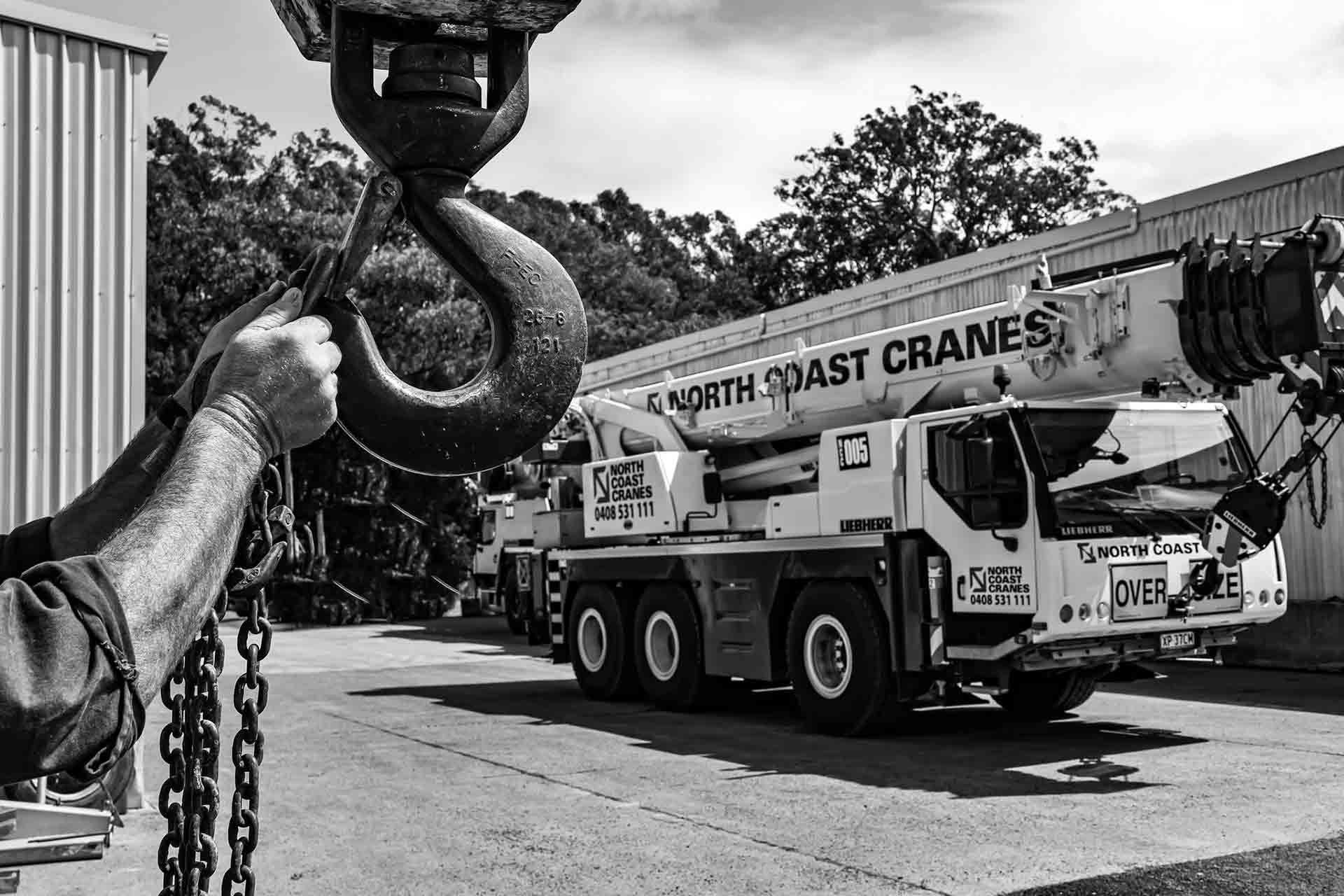 A Black And White Photo Of A Man Holding A Hook Next To A Crane Truck — North Coast Cranes In Armidale, NSW
