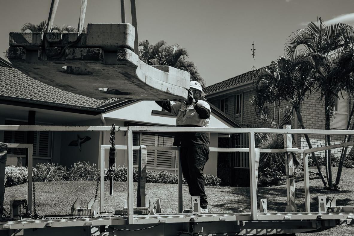 A Black And White Photo Of A Crane Lifting A Concrete Slab Into A House — North Coast Cranes In Coffs Harbour, NSW