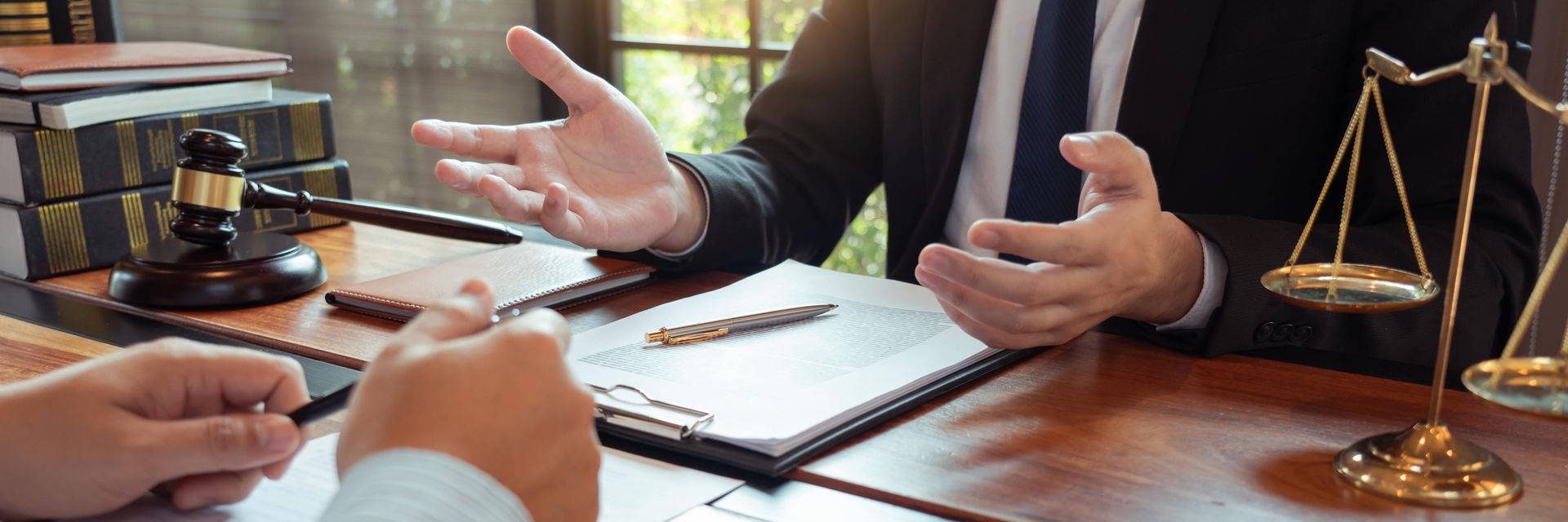 Two people are discussing documents, gavel and scales on a wooden desk.