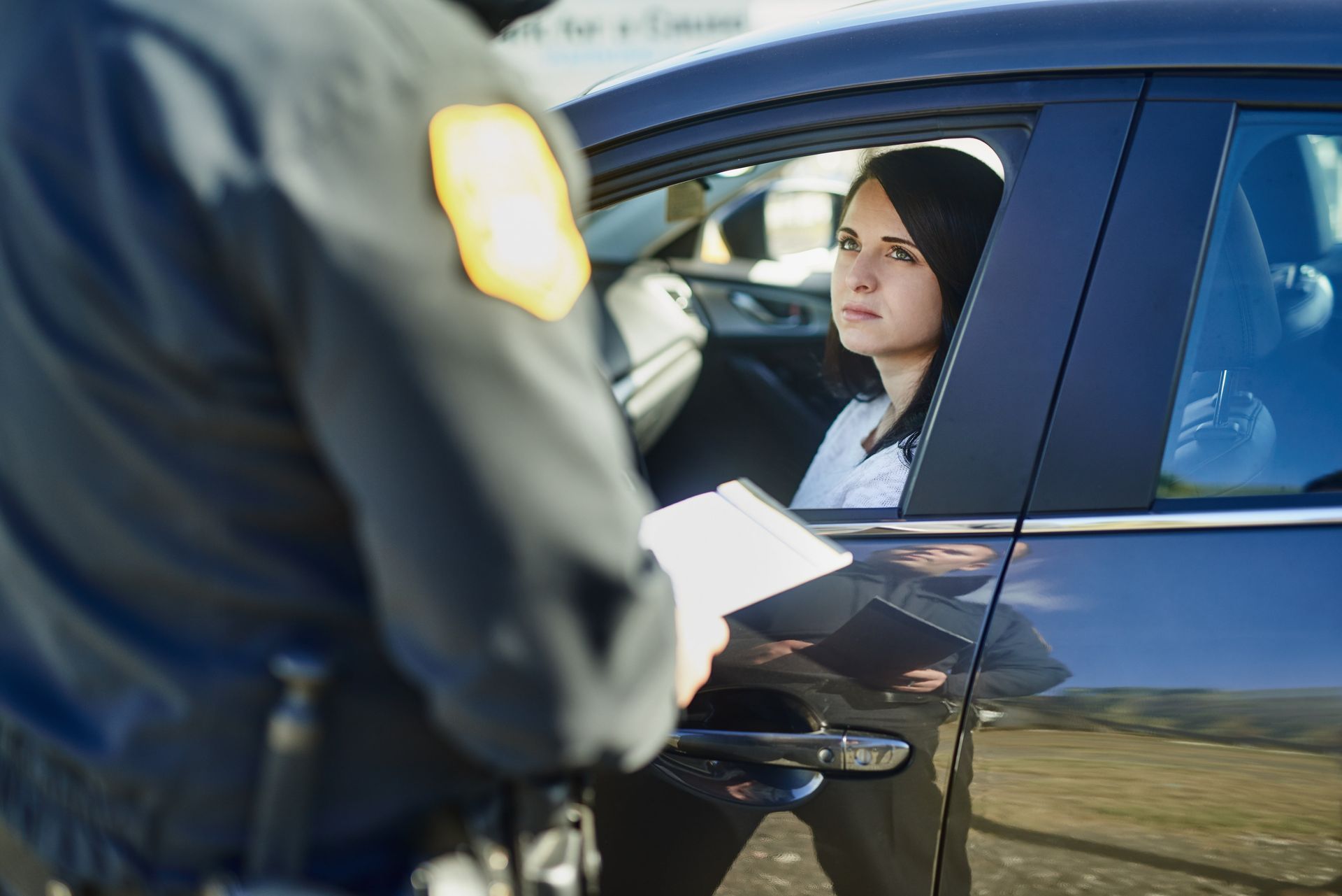 Police officer handing paperwork to a driver in a car.