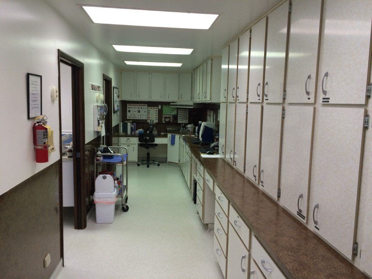 Long hallway in a medical office with white cabinets, a desk, and medical equipment.