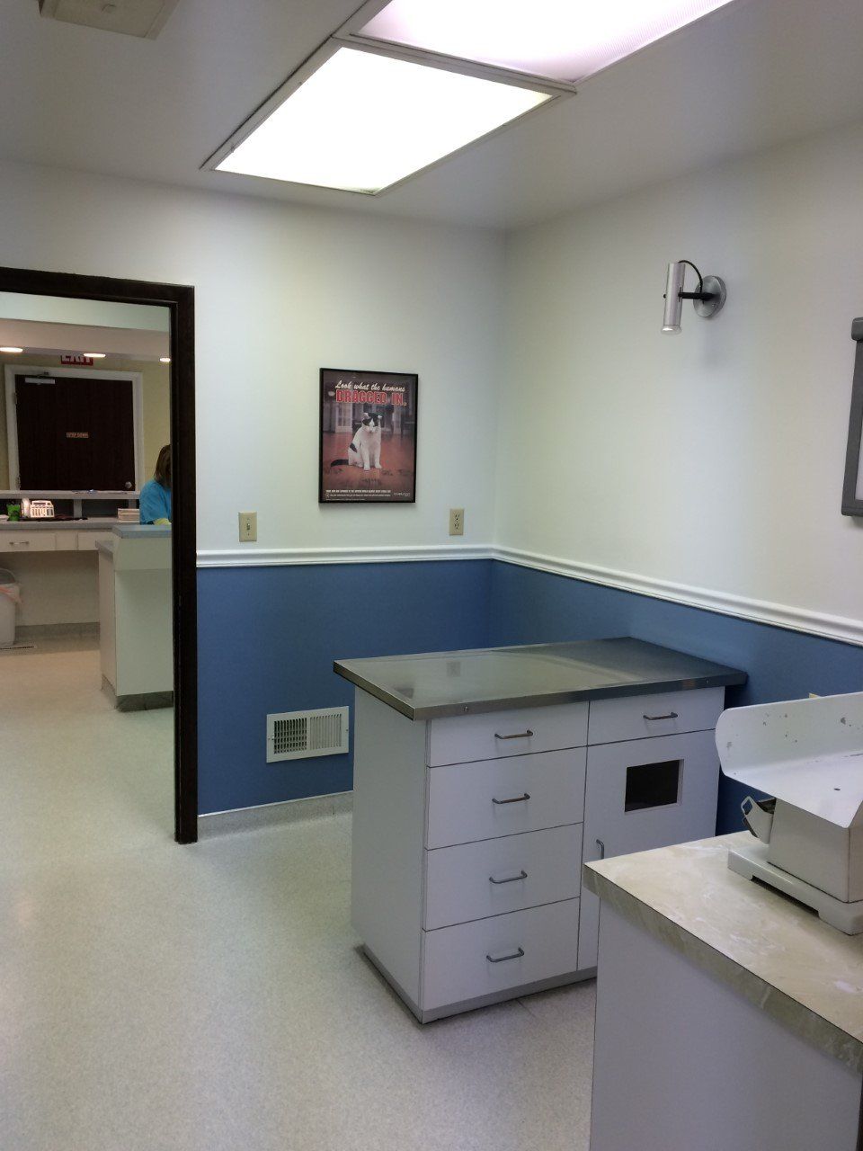 Exam room with blue and white walls, cabinet, and door to a hallway.