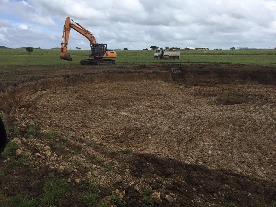 A Large Excavator is Digging a Hole in a Field — Curtis Coast Excavators in Gladstone, QLD
