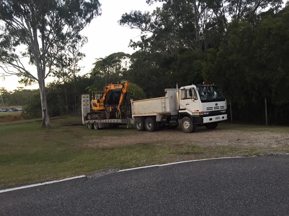 A Dump Truck with a Yellow Excavator on the Back is Parked on the Side of the Road — Curtis Coast Excavators in Gladstone, QLD