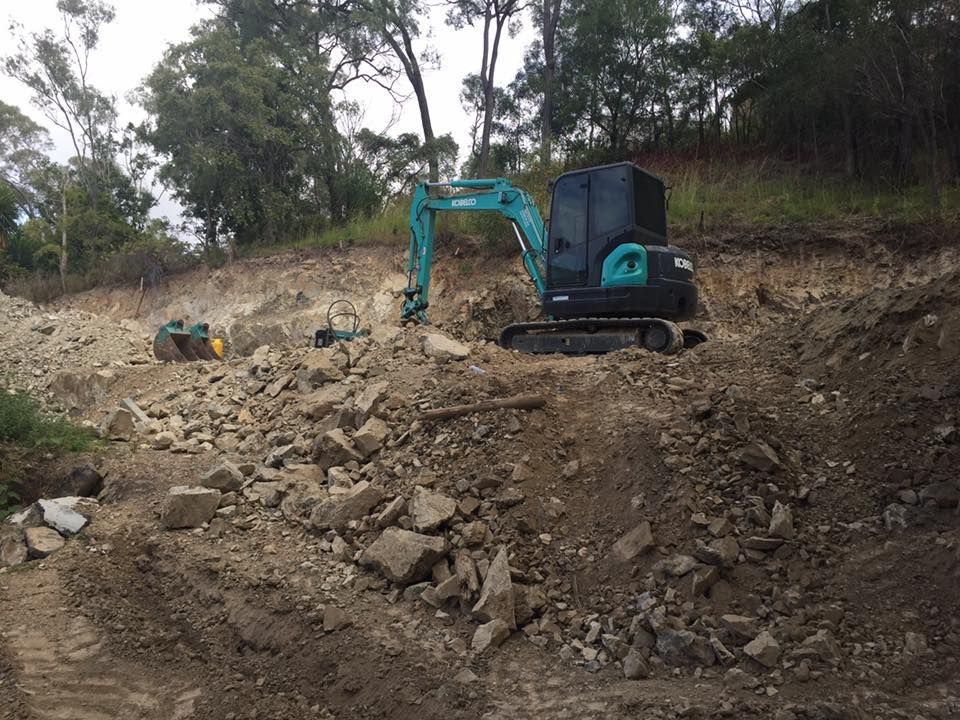A Small Excavator is Sitting on top of a pile of Rocks — Curtis Coast Excavators in Gladstone, QLD