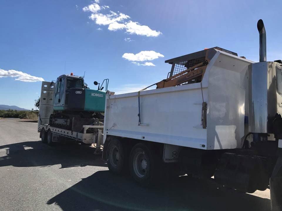 A Dump Truck is Carrying a Green Excavator on a Trailer — Curtis Coast Excavators in Gladstone, QLD