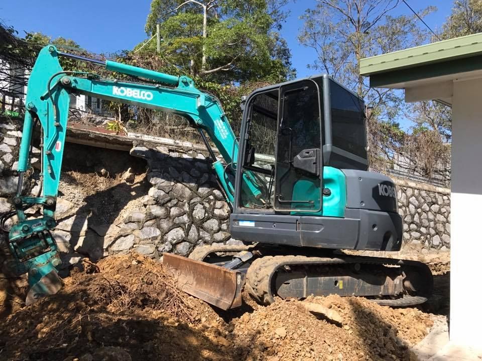 A Small Excavator is Digging a hole in the dirt in front of a House — Curtis Coast Excavators in Gladstone, QLD