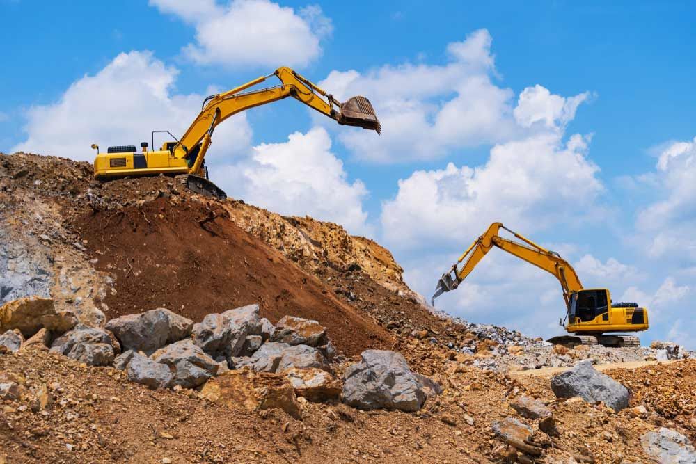 Two Yellow Excavators are Working on a Rocky Hillside — Curtis Coast Excavators in Gladstone, QLD