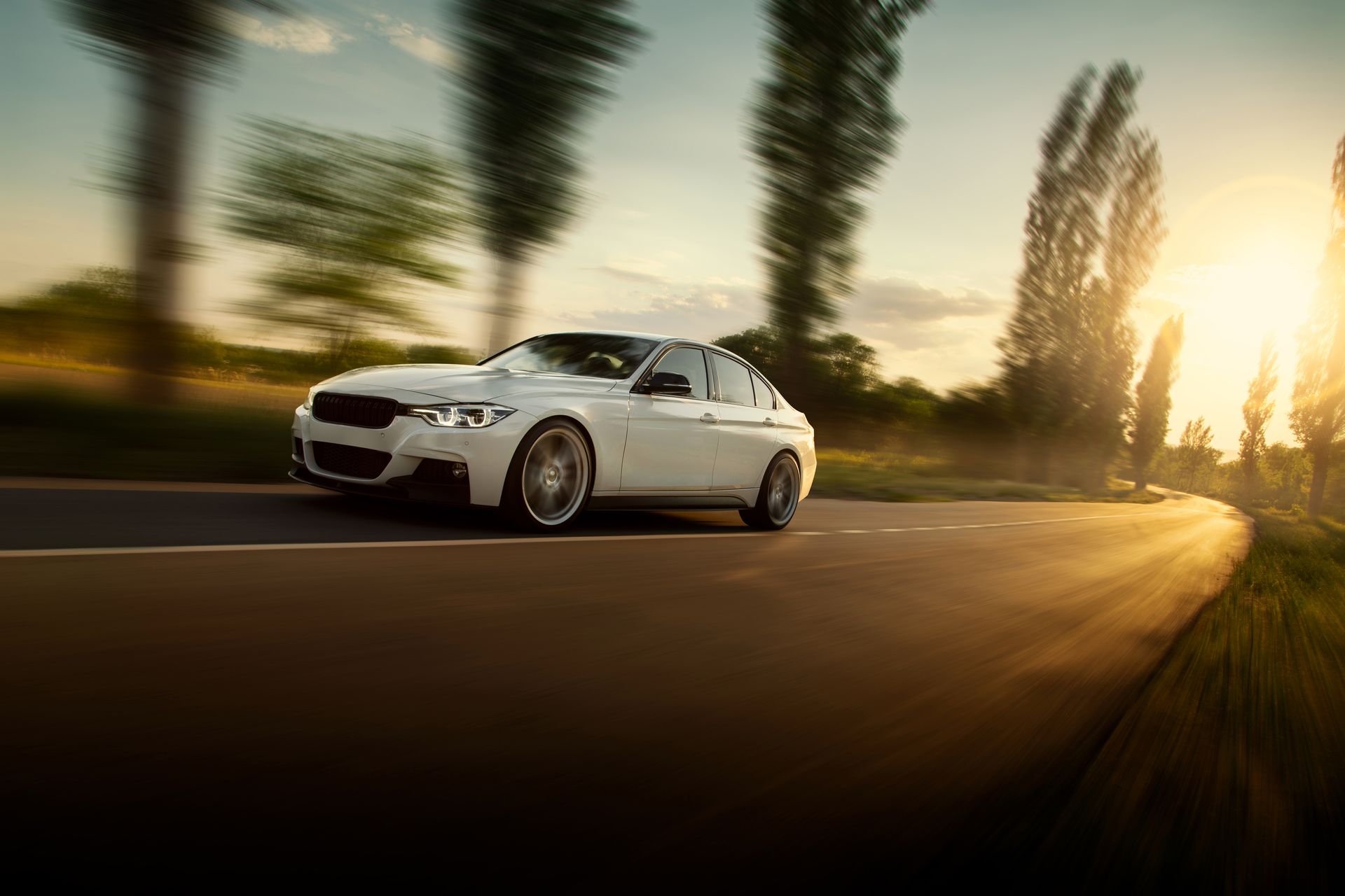 A white car is driving down a country road at sunset