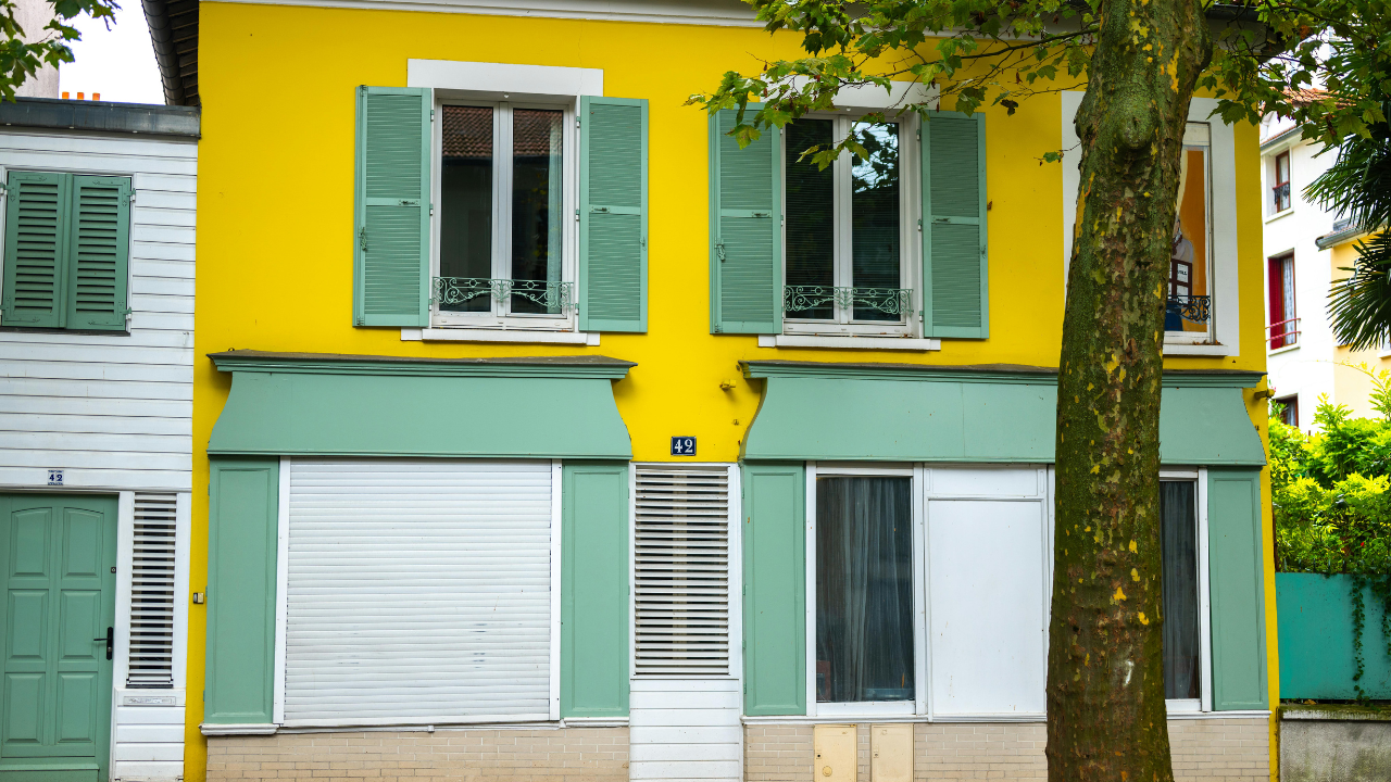 Yellow building with green shutters and awnings; white and green accents.