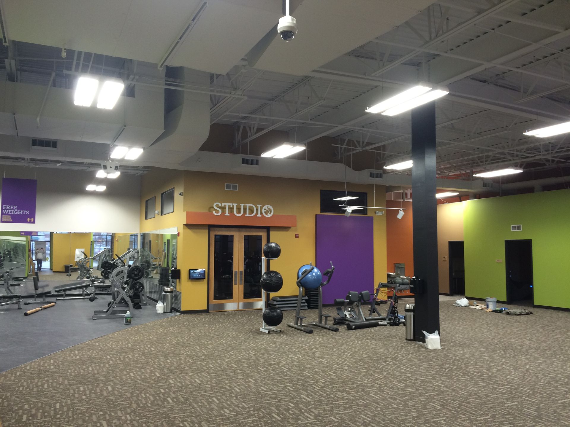 A person paints a house window trim, standing on the roof under a blue sky.