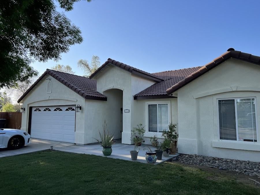 Beige house with a tile roof, a white garage door, and a grassy lawn under a clear, blue sky.