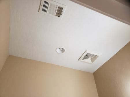 White ceiling with ventilation and a light fixture, above tan walls.