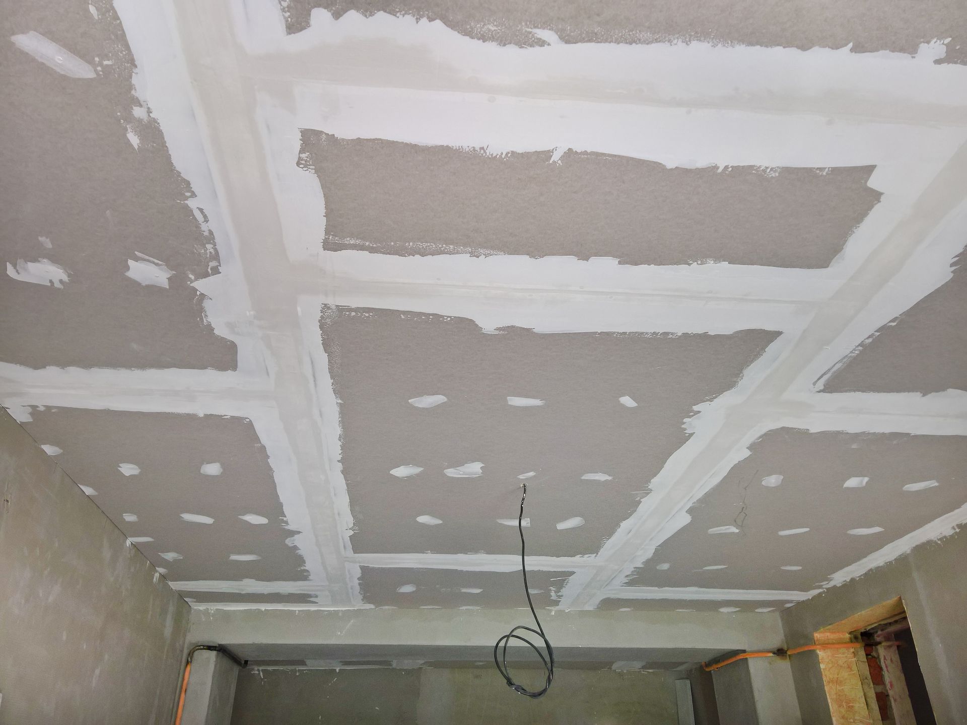 Drywall ceiling with white joint compound filling the seams, in a room under construction.