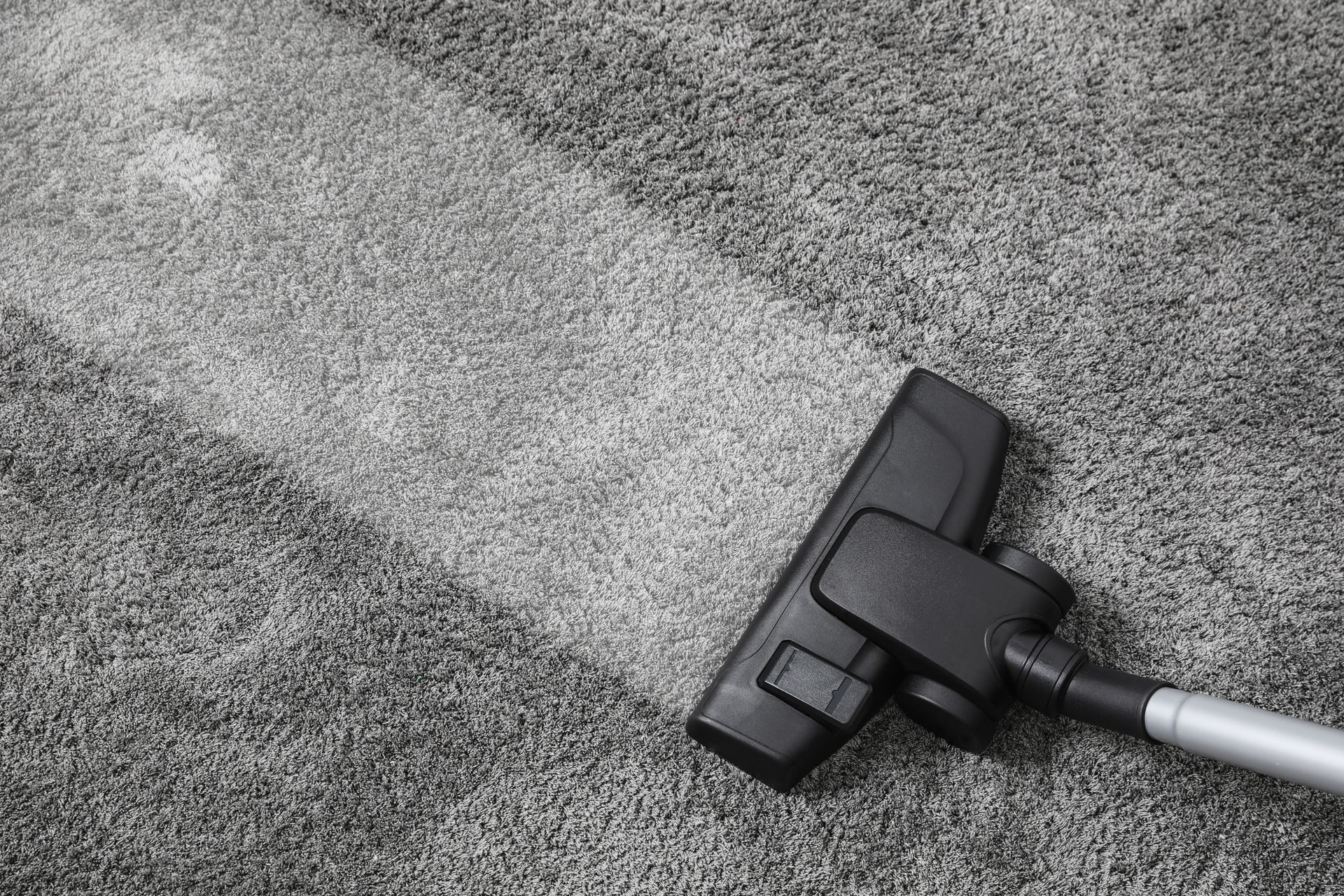 Vacuum cleaner cleaning gray carpet, leaving a clean path.