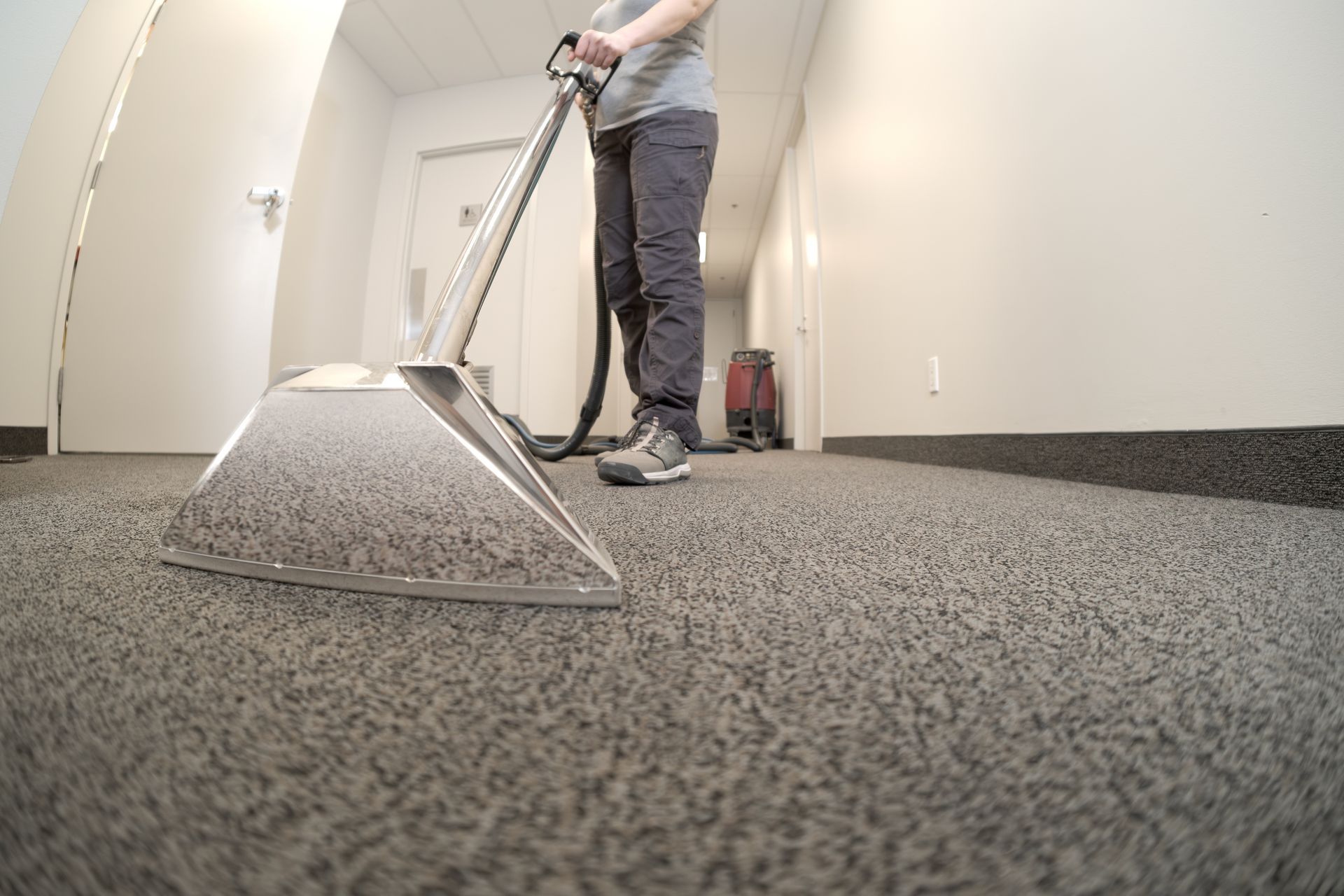 Person vacuuming hallway carpet with a professional machine.