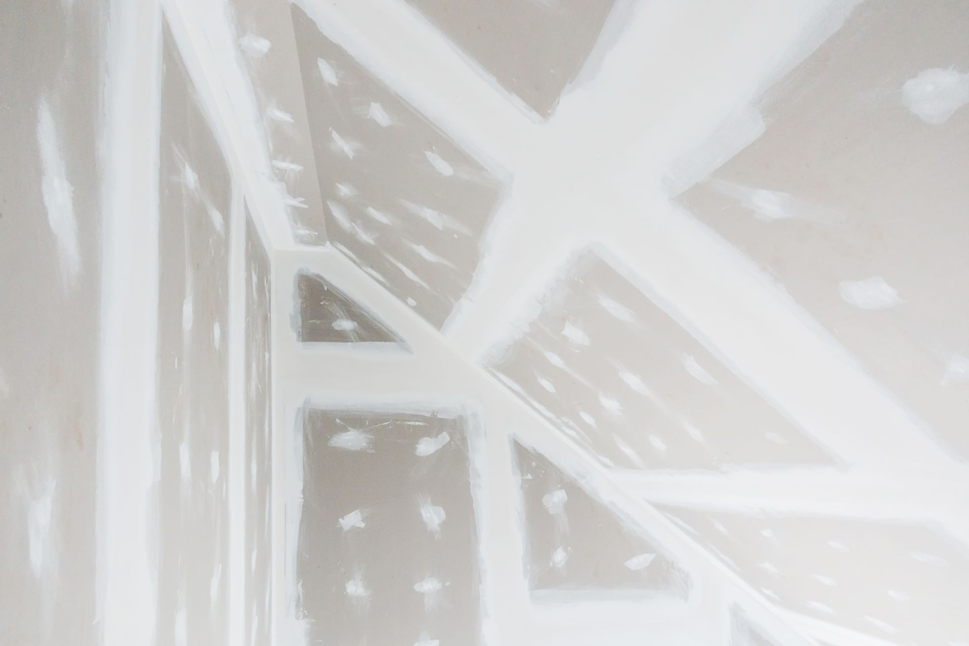 Interior of a room with drywall installed. White drywall tape and compound cover seams and screw holes.