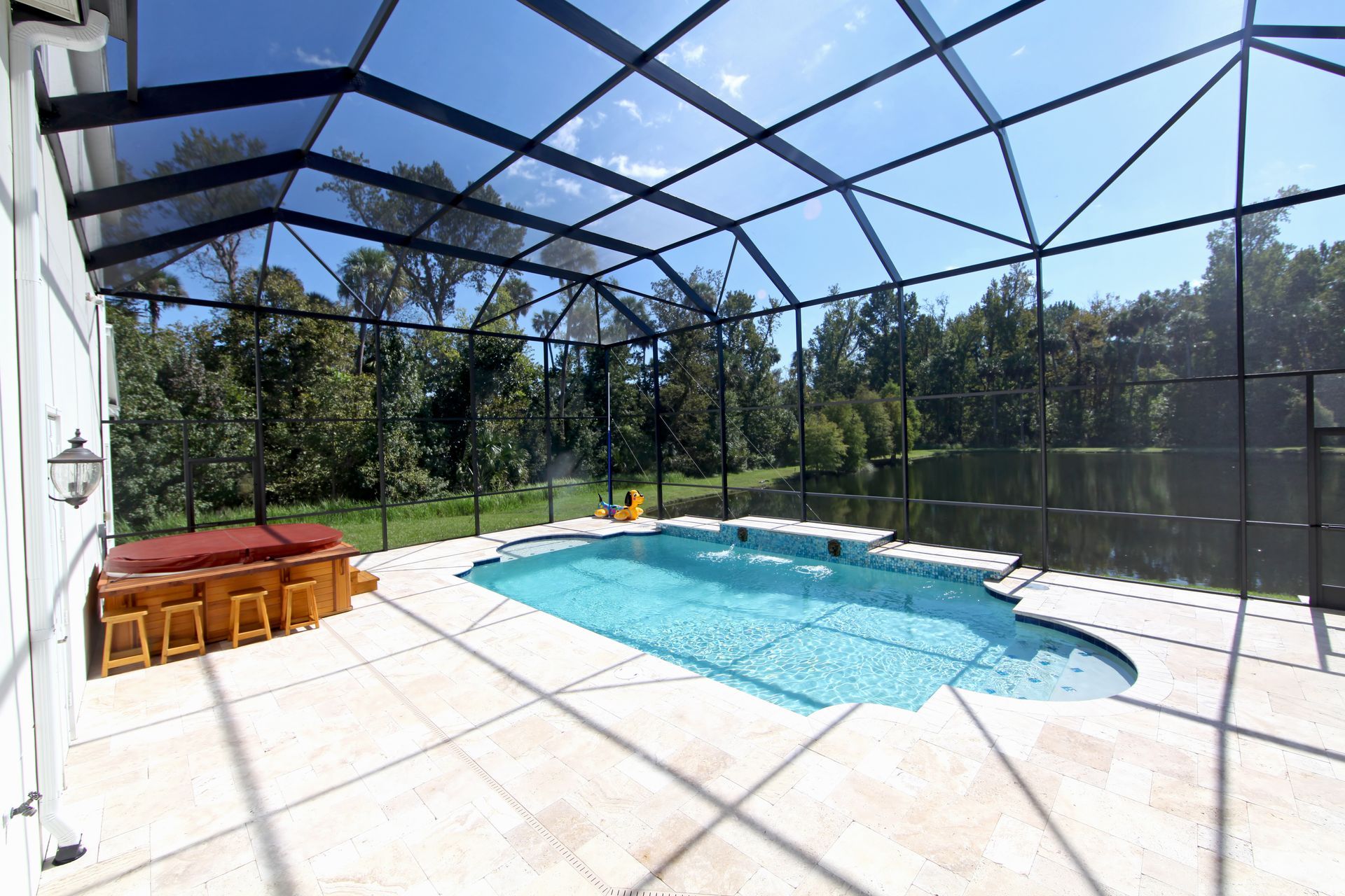 Pool and hot tub enclosed in a screened patio, bright blue sky, trees in the background.