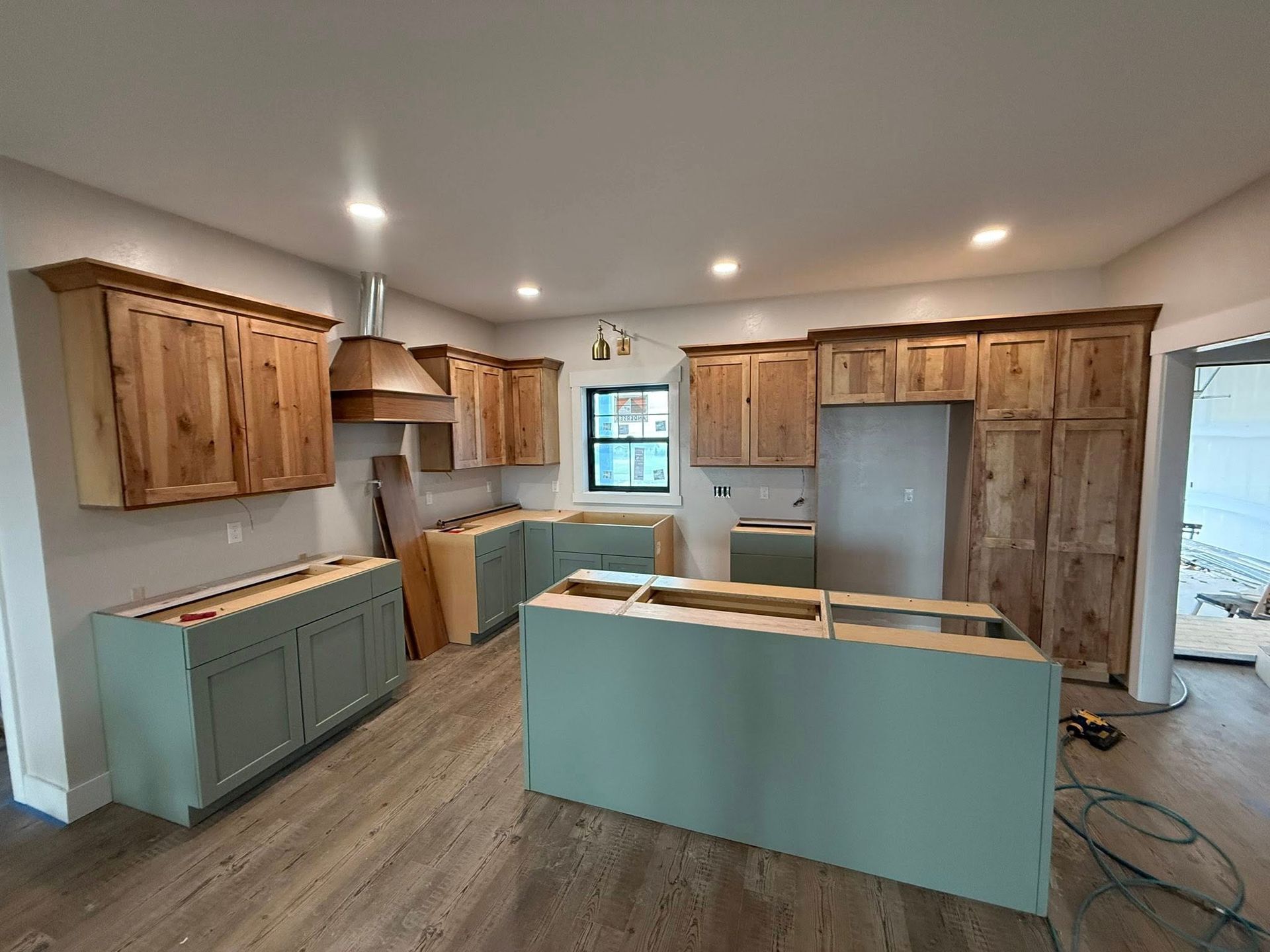 Kitchen under construction with light green cabinets and natural wood uppers; stainless steel appliances.