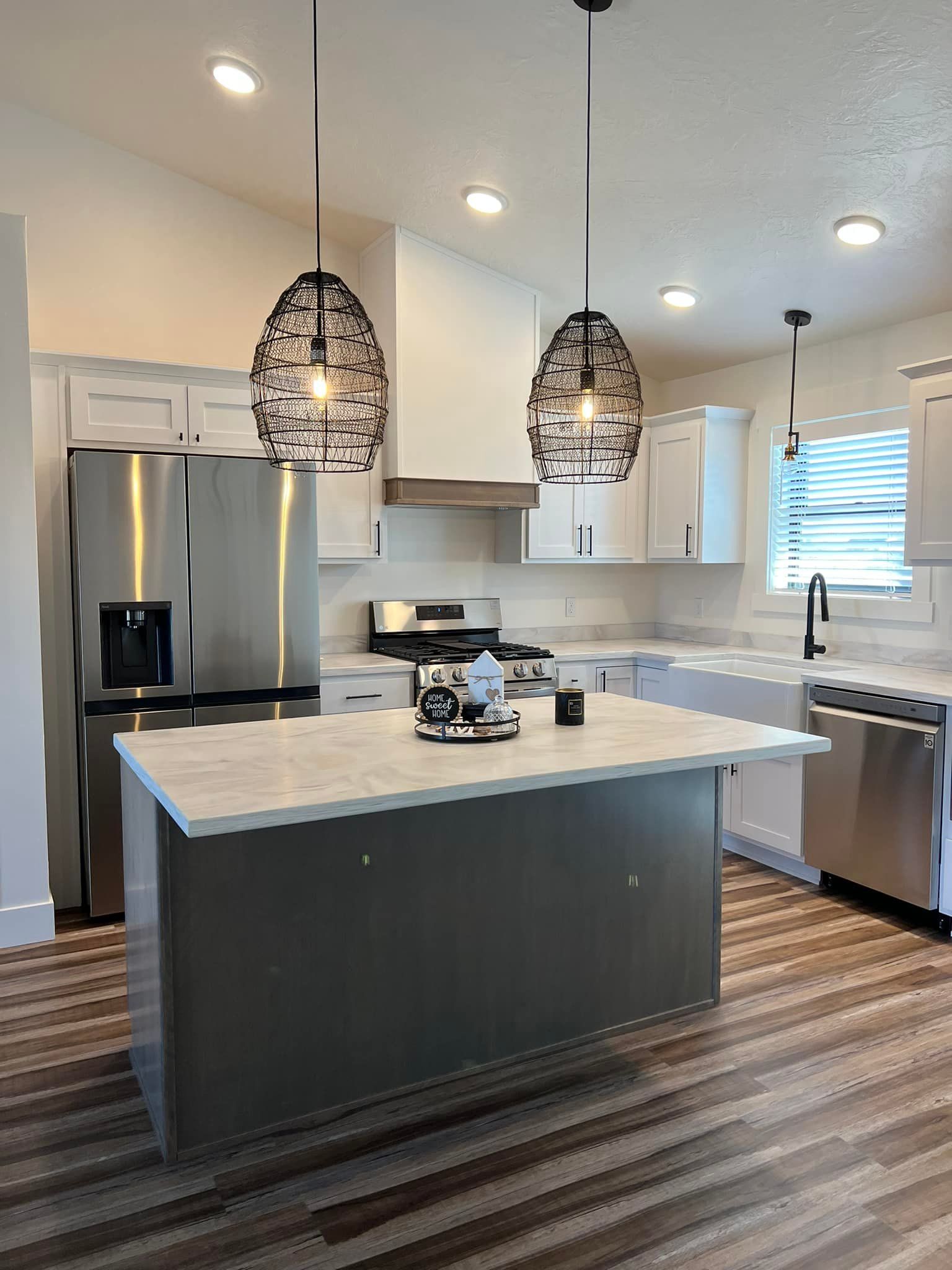 Modern kitchen with gray island, white cabinets, stainless steel appliances, and pendant lights.