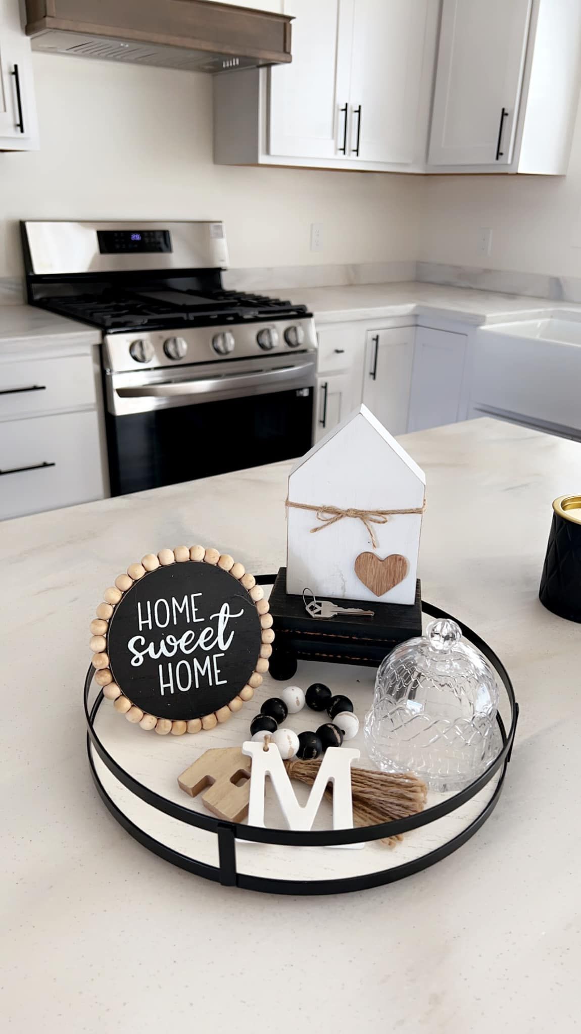 Tray with home decor on a kitchen countertop, including a chalkboard sign, a house-shaped ornament, and a clear glass orb.