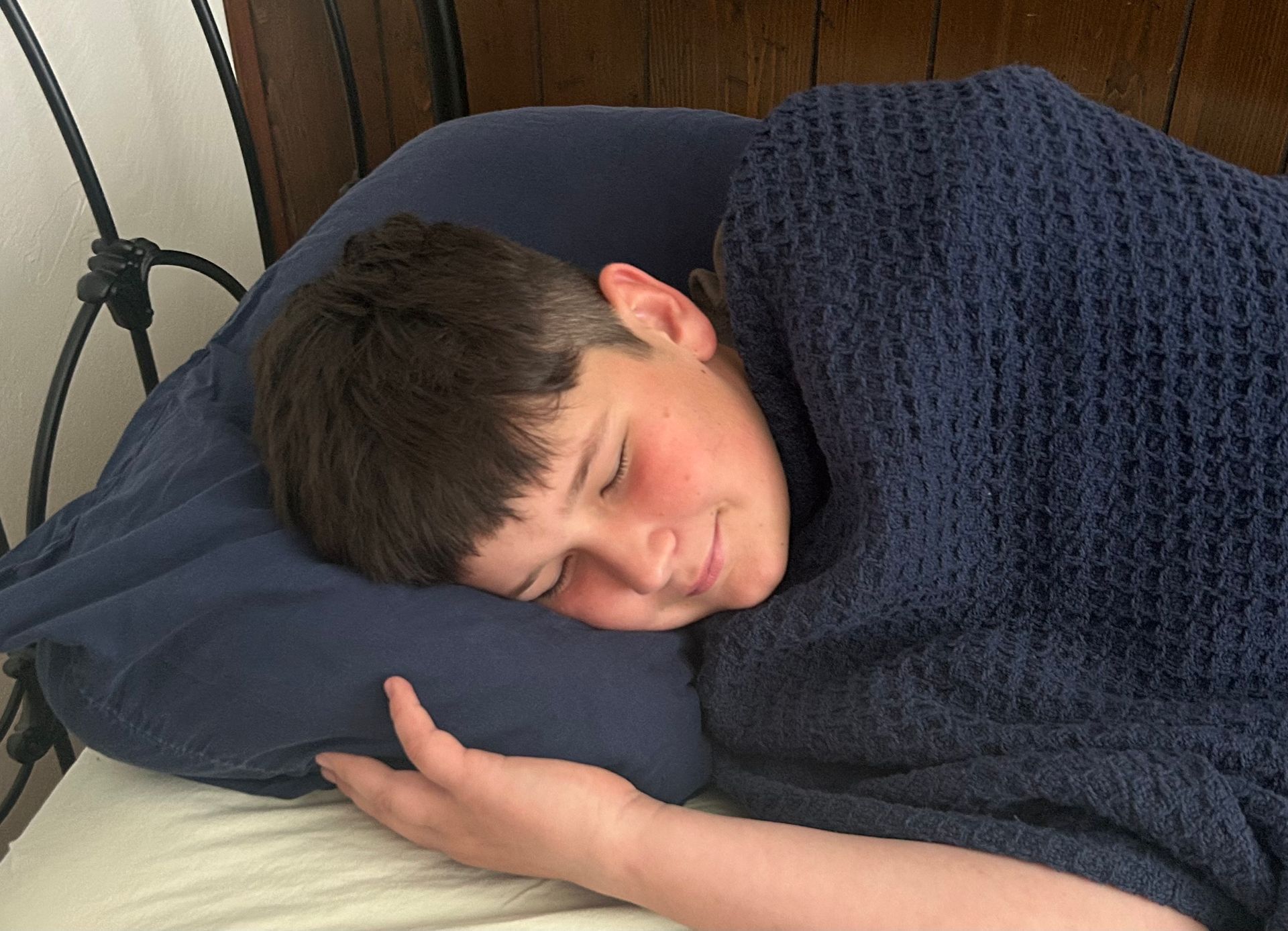 Boy sleeping in bed, covered by a blue blanket and resting head on a blue pillow.