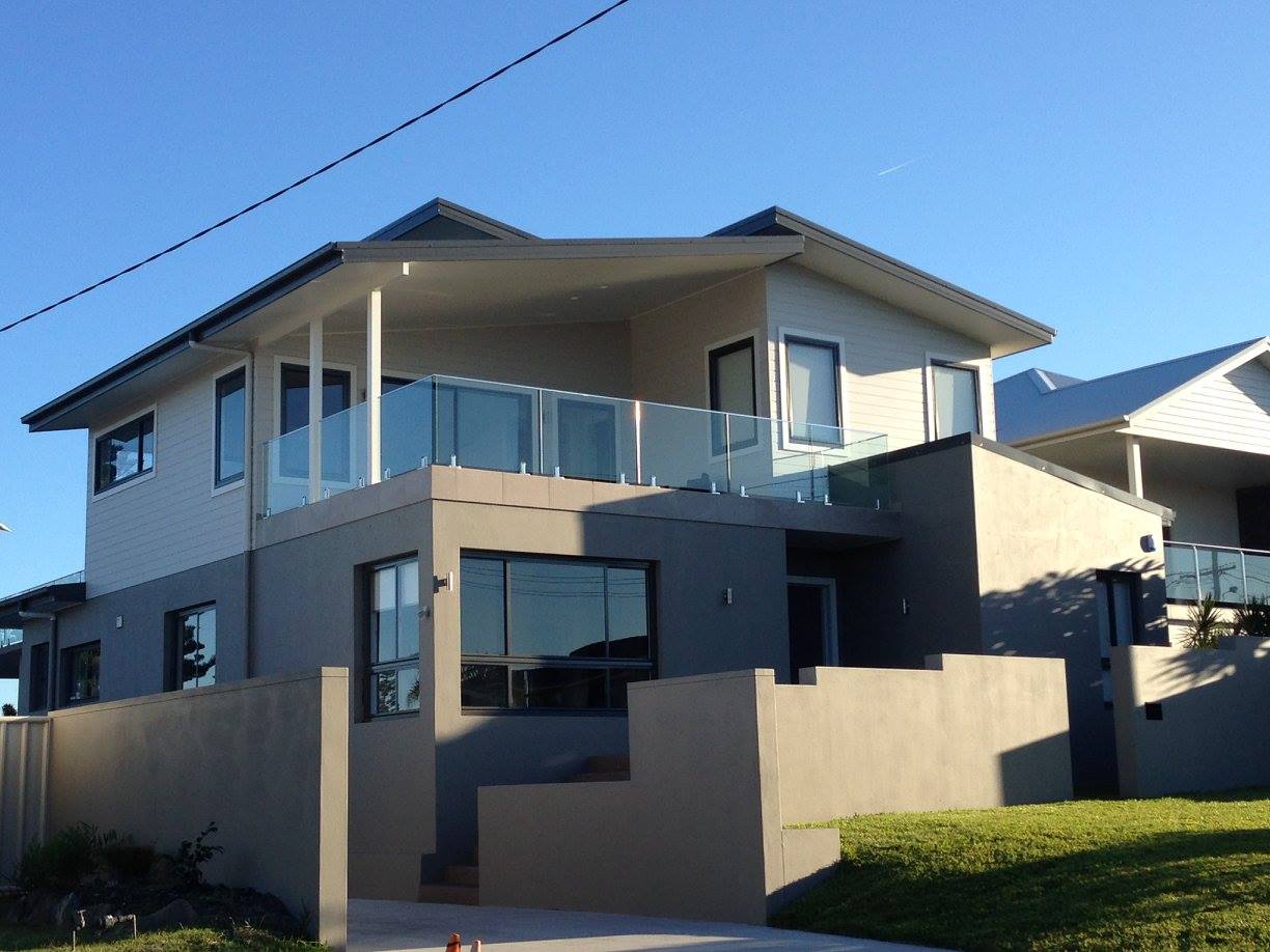 Two-story modern house with glass balconies and gray exterior against a blue sky.