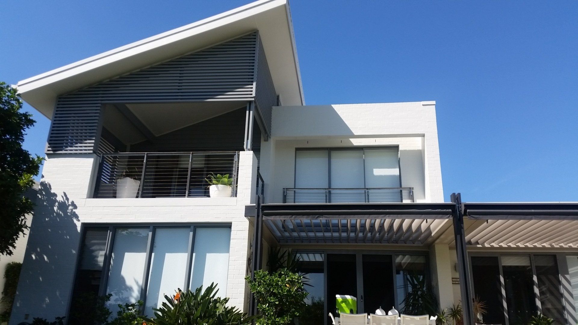 Modern white townhouse with balcony, plants, and blue sky.
