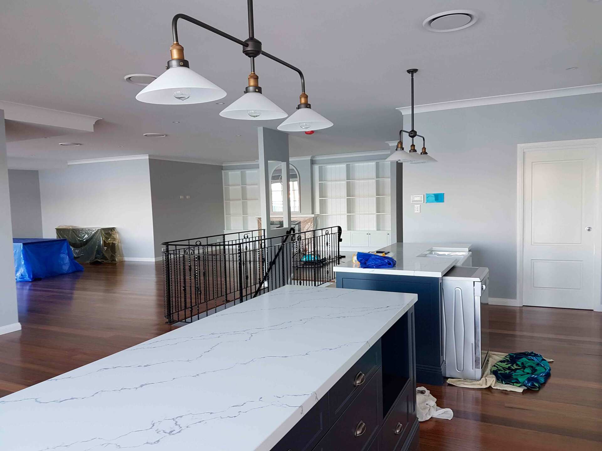 Kitchen with a large island, pendant lights, and wood floors. Dark blue cabinets, white countertops, and gray walls.