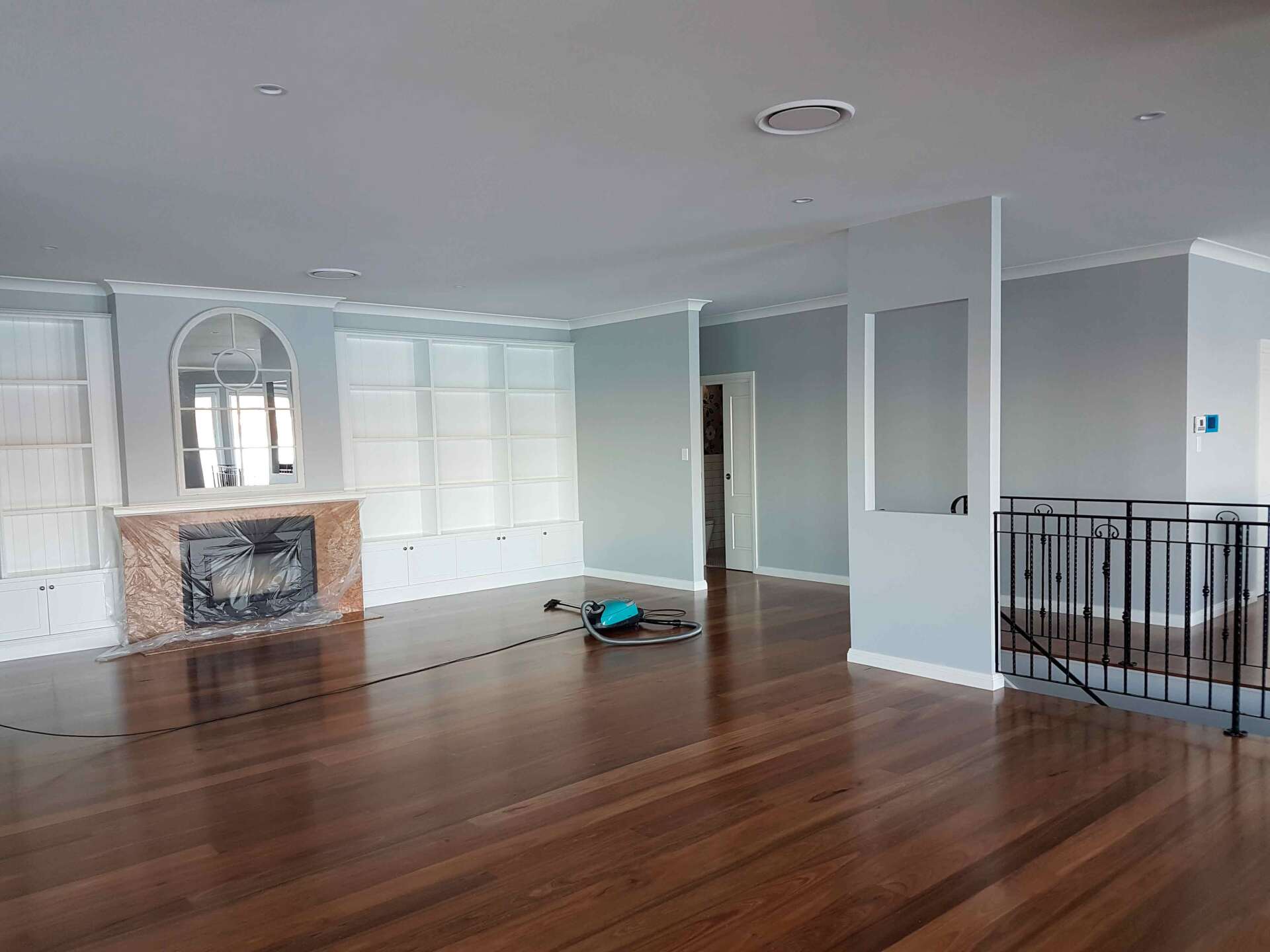 Empty living room with hardwood floors, fireplace, built-in shelves, and light blue walls.