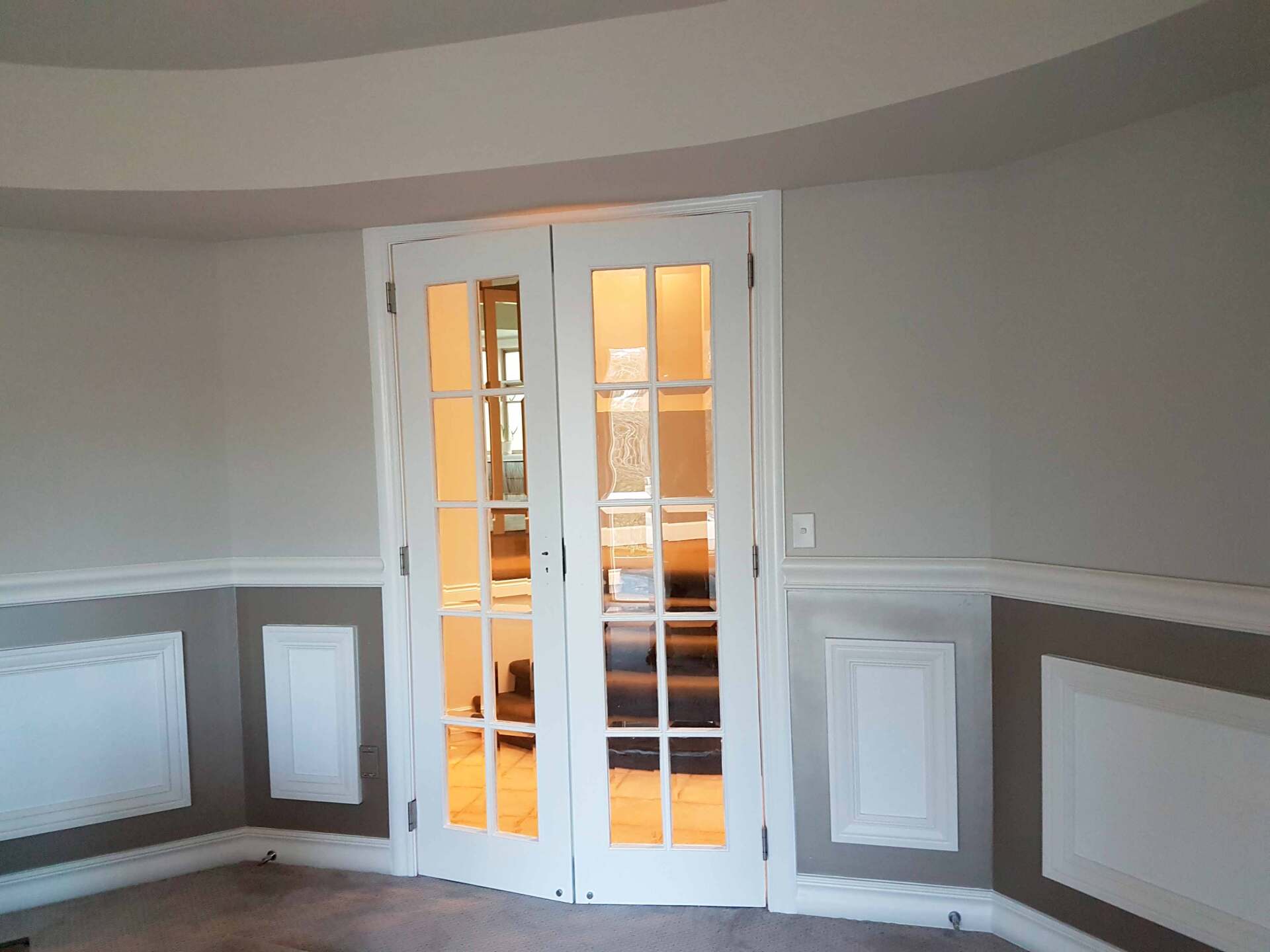 White french doors in a room with gray and white paneling. The room appears to have curved walls and ceilings.