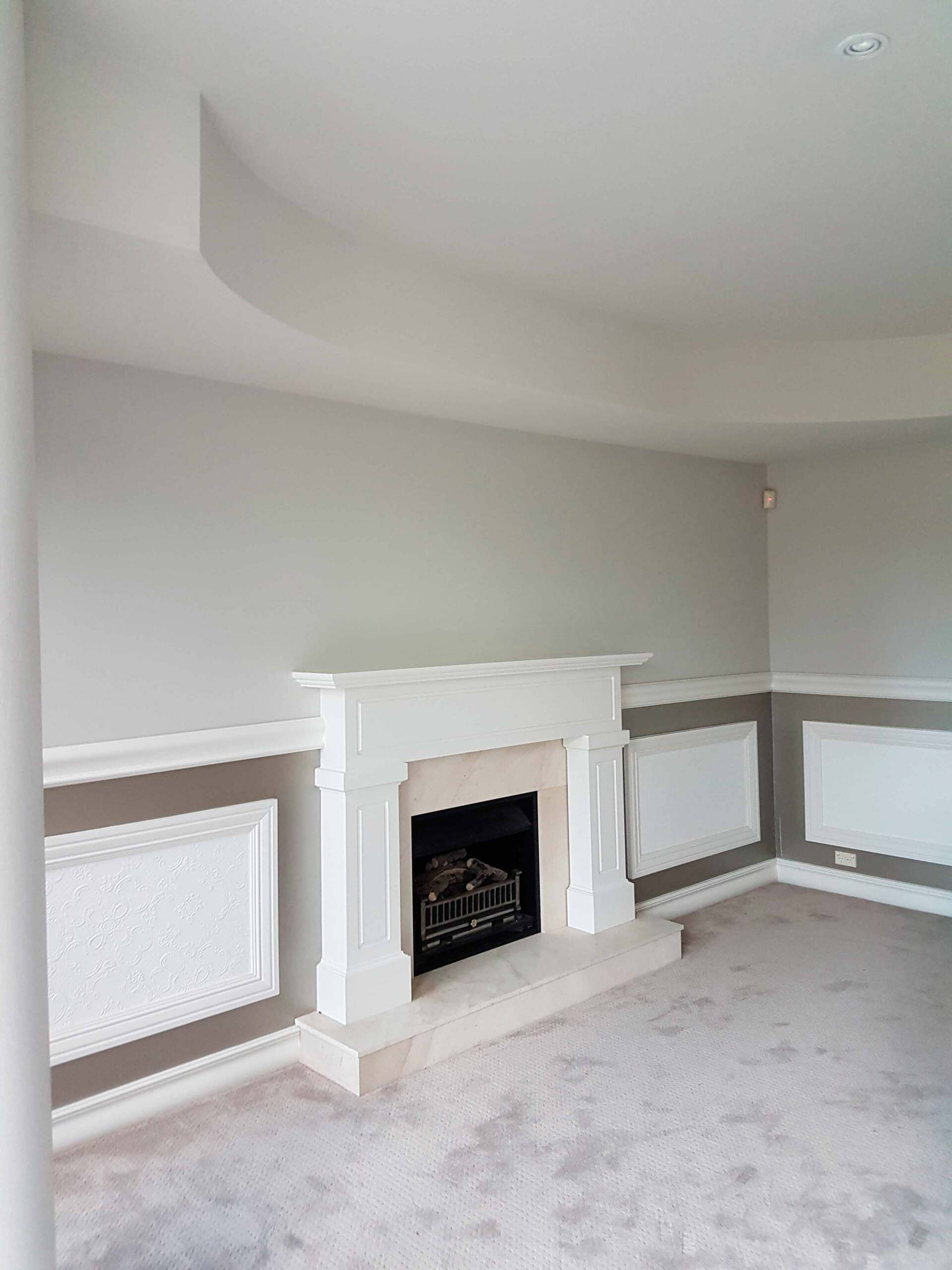 A living room with a fireplace, gray walls, white trim and molding, and carpet.